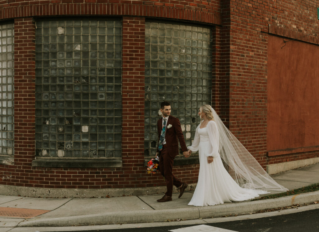 bride and groom walking around a brick building together, holding hands