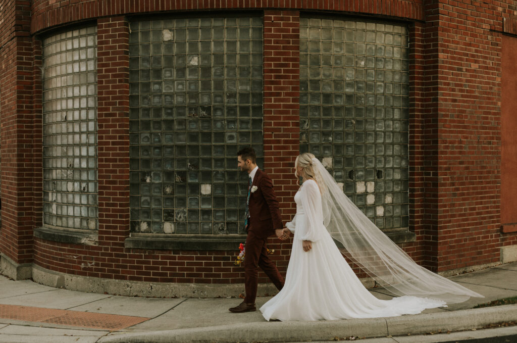 upscale bride and groom portraits outside of historical wedding venue with square glass brick wall and colorful floral bouquet