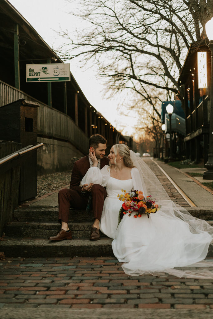 upscale bride and groom portraits outside of historical wedding venue during golden hour with sparkling lights and colorful wedding bouquets sitting on stairs