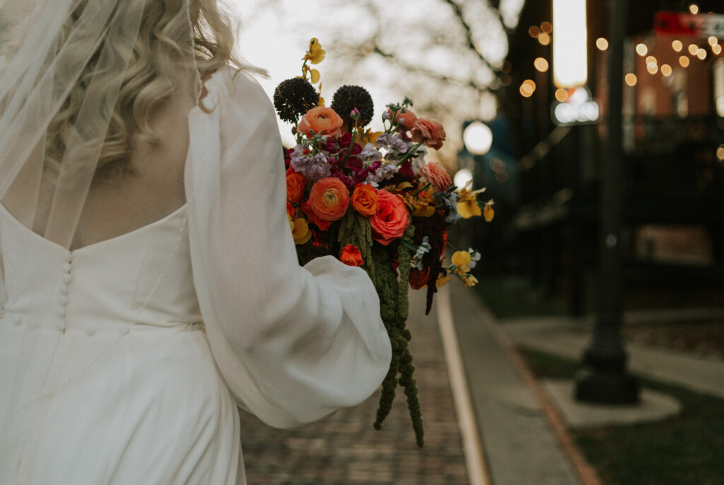 upscale bride and groom portraits outside of historical wedding venue during golden hour with sparkling lights and colorful wedding bouquets