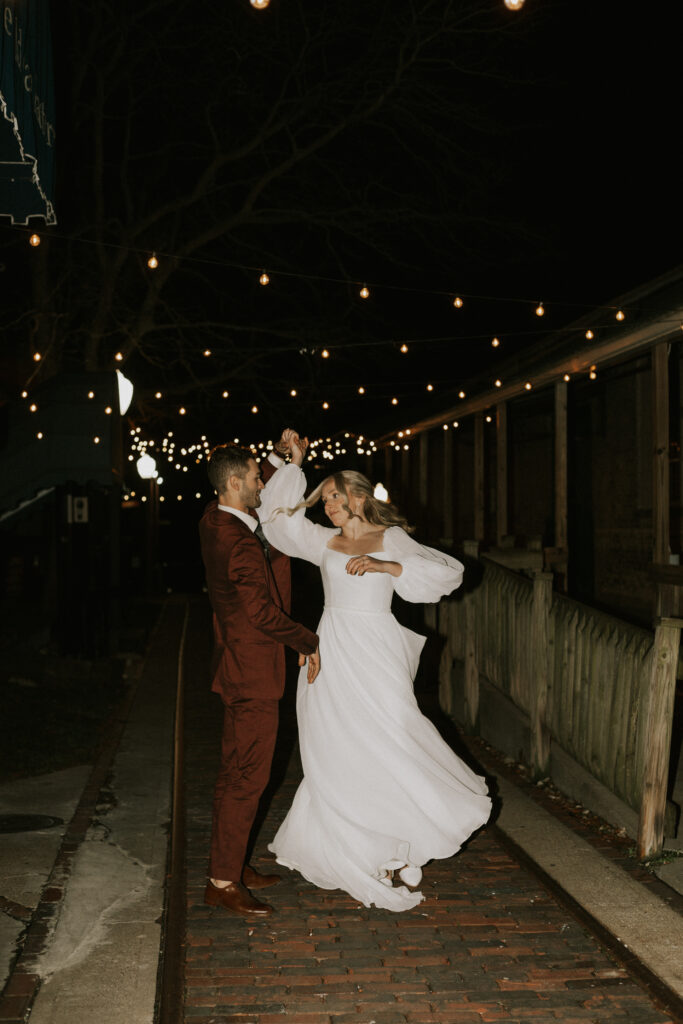 upscale bride and groom portraits outside of historical wedding venue during golden hour with sparkling lights, flash photography of bride and groom spinning and twirling