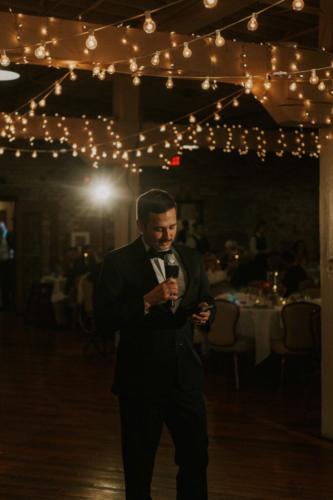 speeches at wedding reception by best man in historical wedding venue with sparkling lights