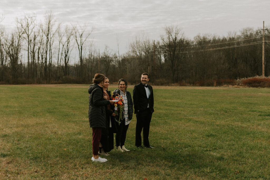 first look with bride and groom on wedding day in a large field surrounded by foliage and family members