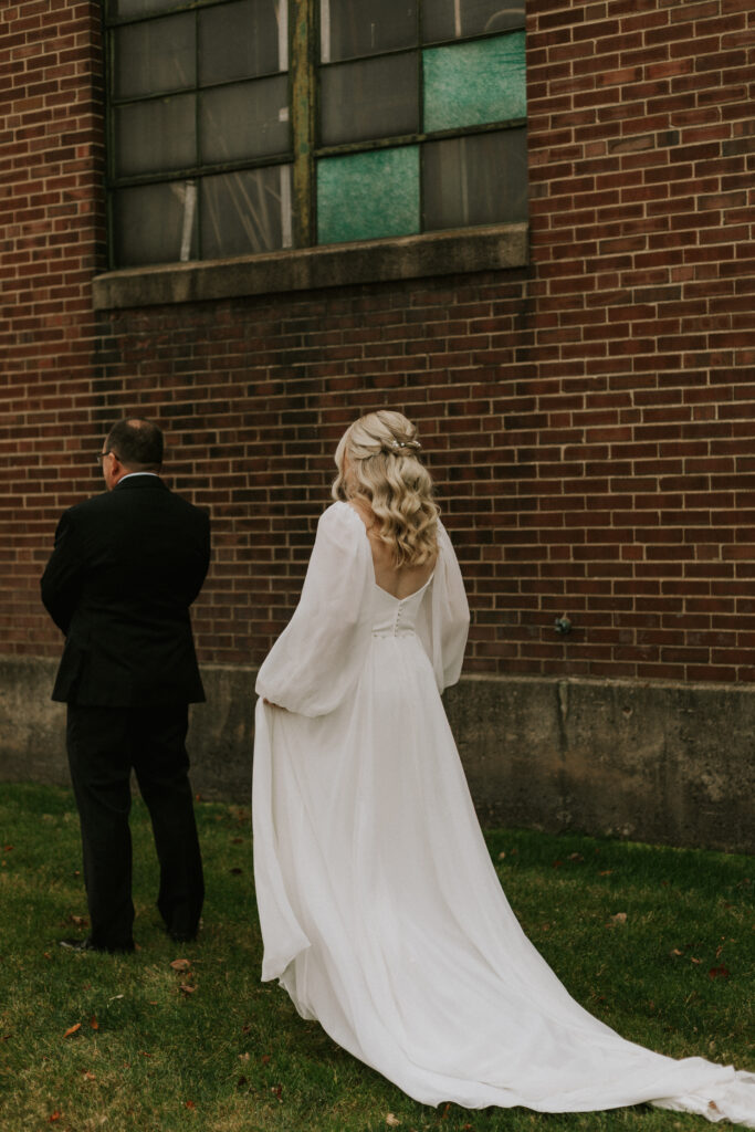 first look with bride and father of the bride in a field with a historical brick building with stained glass