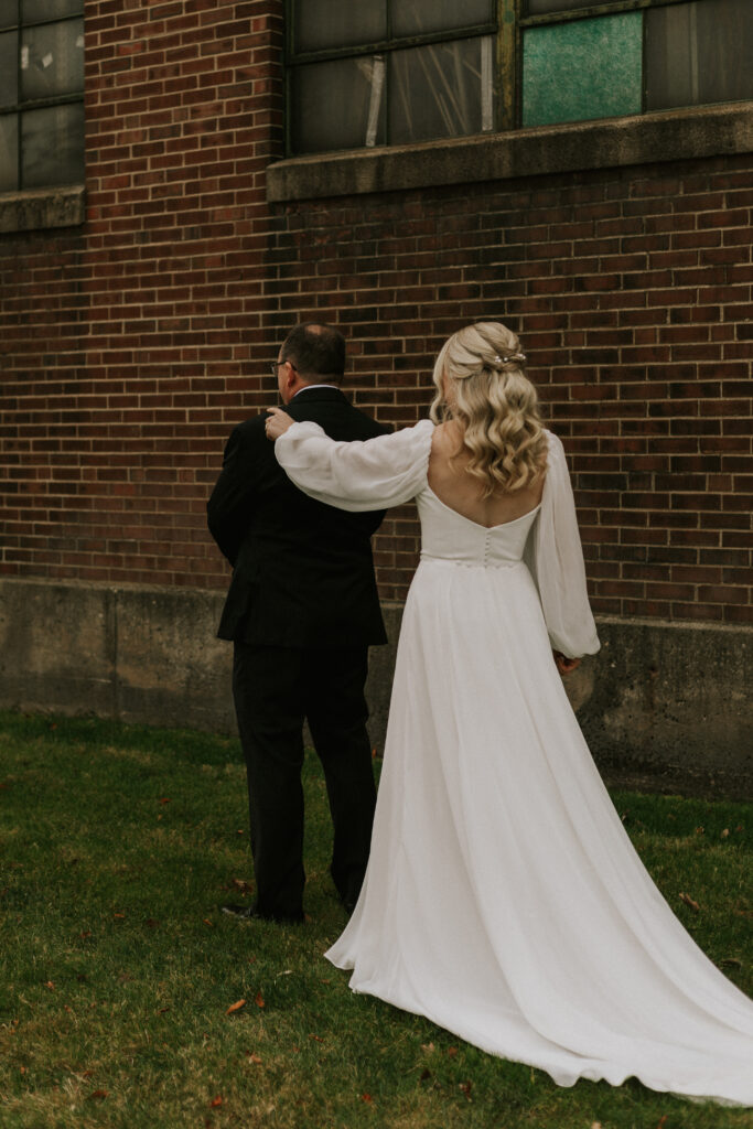 first look with bride and father of the bride in a field with a historical brick building with stained glass