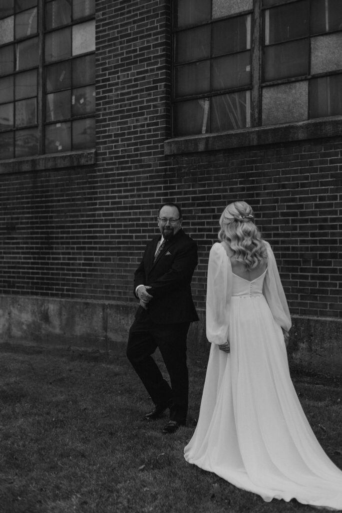 first look with bride and father of the bride in a field with a historical brick building with stained glass, father of bride sees bride for the first time