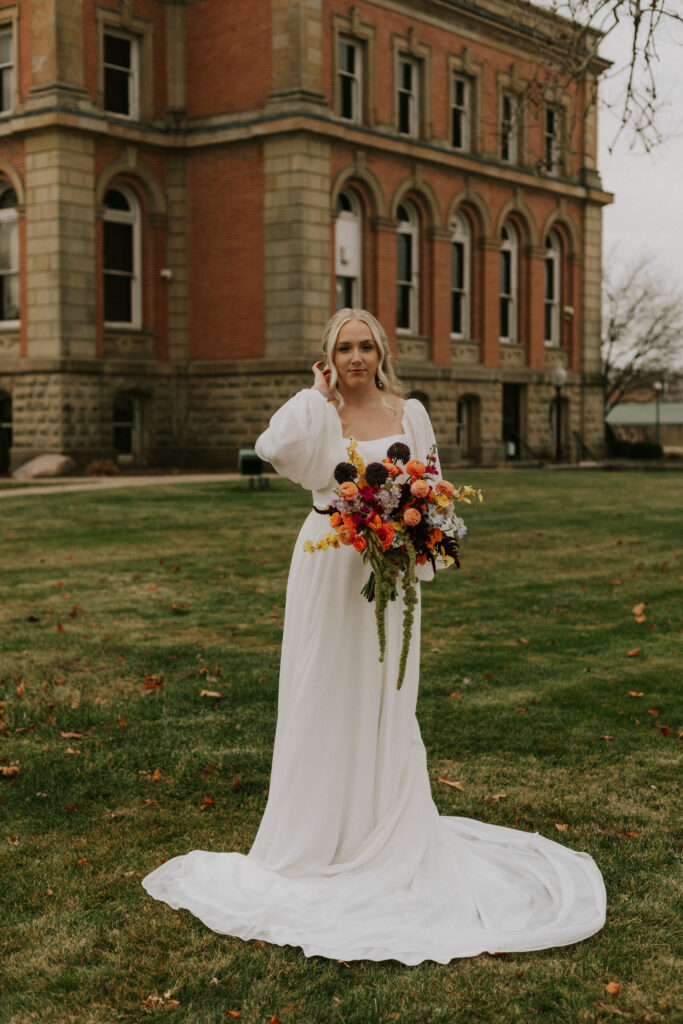 bride portraits at Goshen, Indiana courthouse downtown Goshen on steps with historical building in background holding colorful bouquet