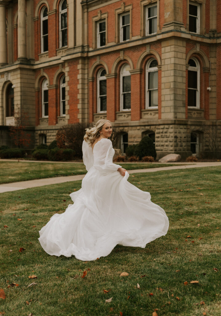 bride portraits at Goshen, Indiana courthouse downtown Goshen on steps with historical building in background, bride is running away from camera with dress flowing in the wind