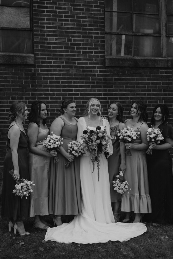 bridal party pictures taken in front of a historical brick building in downtown Goshen Indiana with iron windows and colorful bridemaid dresses and bouquets 