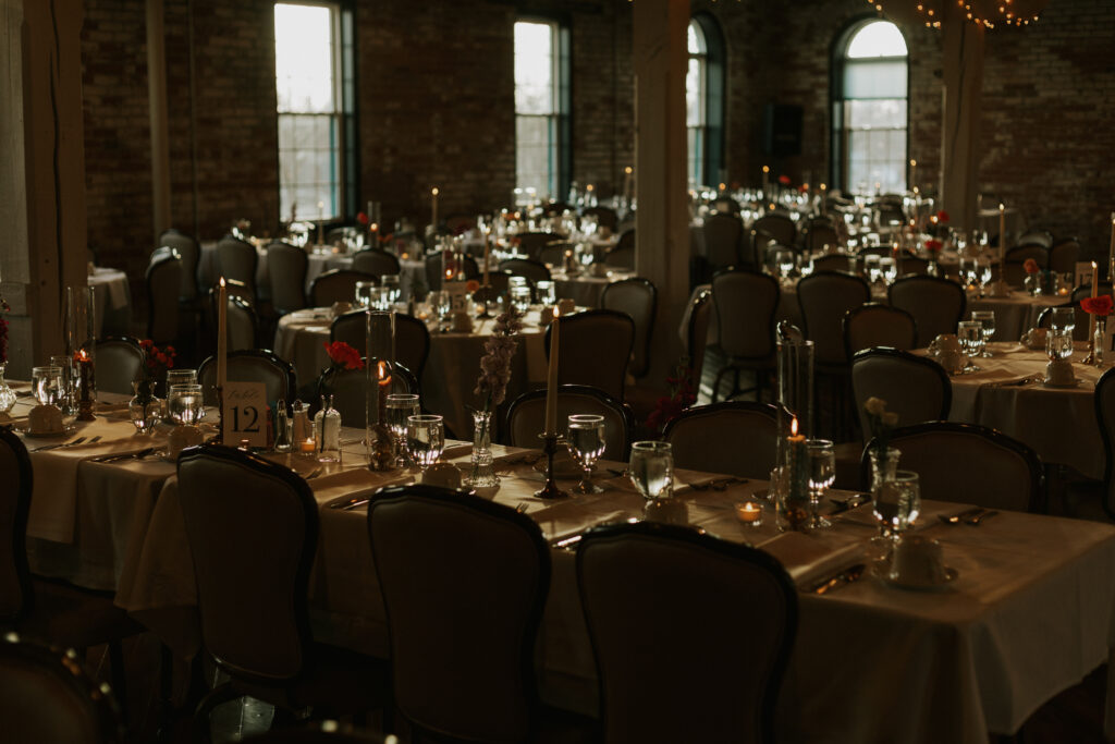 moody brick wedding venue Bread & Chocolate table details with glasses, candle sticks, flowers in vases, and tealights