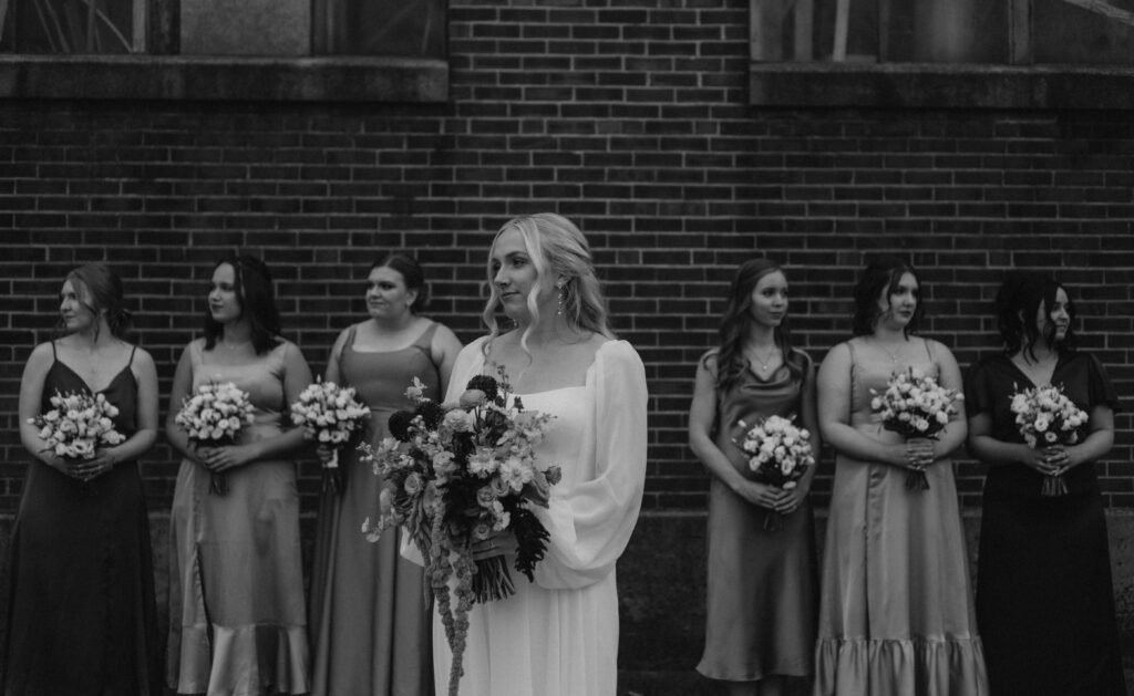 bridal party pictures taken in front of a historical brick building in downtown Goshen Indiana with iron windows and colorful bridemaid dresses and bouquets 