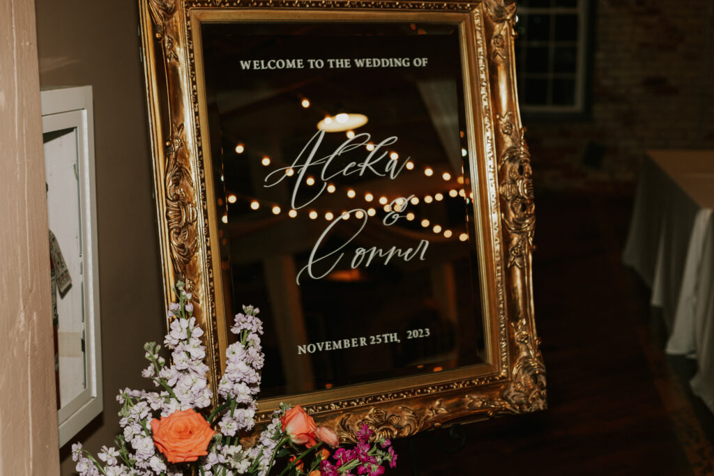 wedding entrance signage with bride and groom names in handwritten calligraphy on a vintage gold mirror