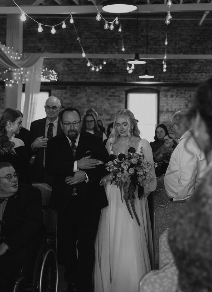 Wedding ceremony processional pictures at Goshen Indiana wedding venue at Bread & Chocolate, bride and father of bride walking down aisle emotional and embracing
