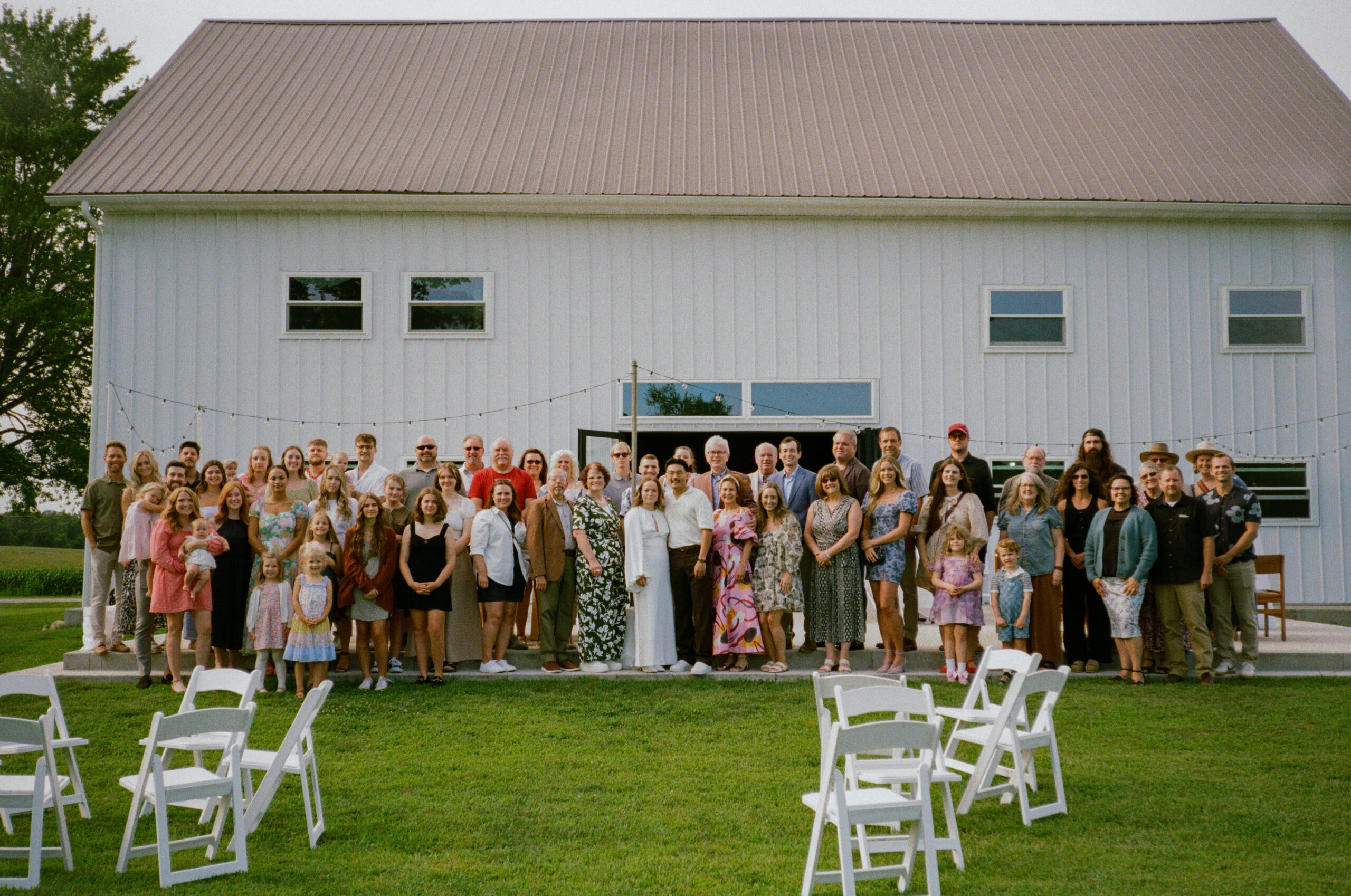 bride and groom's large family photograph standing at their reception space, after their wedding reception, captured on 35mm film in Warsaw and Winona Lake Indiana.