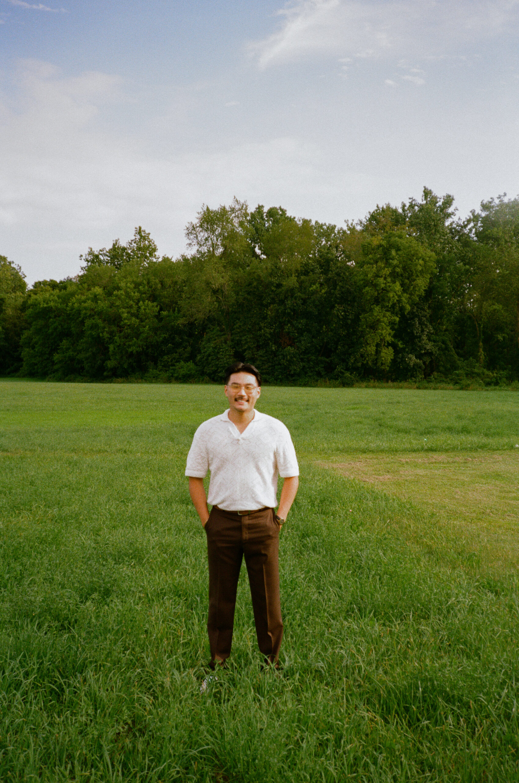 Groom portraits at wedding reception on 35mm film in meadow field, at golden hour, outside of outdoor wedding reception.