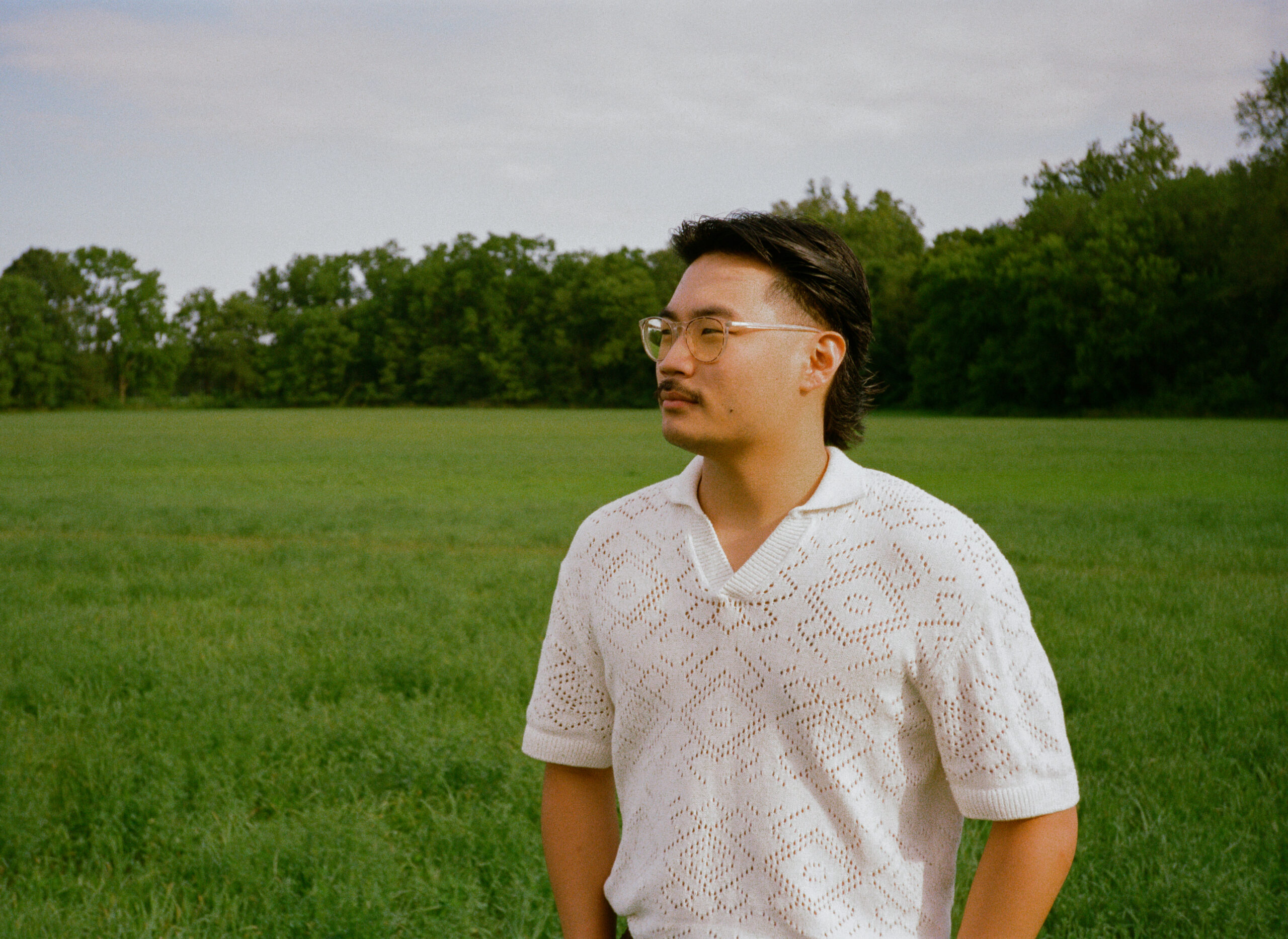 Groom portraits at wedding reception on 35mm film in meadow field, at golden hour, outside of outdoor wedding reception.