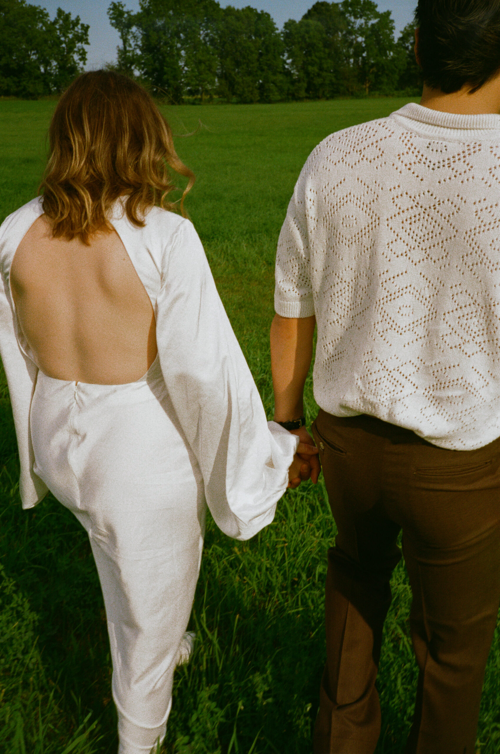 bride and groom photograph standing in a field and walking away together, during golden hour after their wedding reception, captured on 35mm film in Warsaw and Winona Lake Indiana.