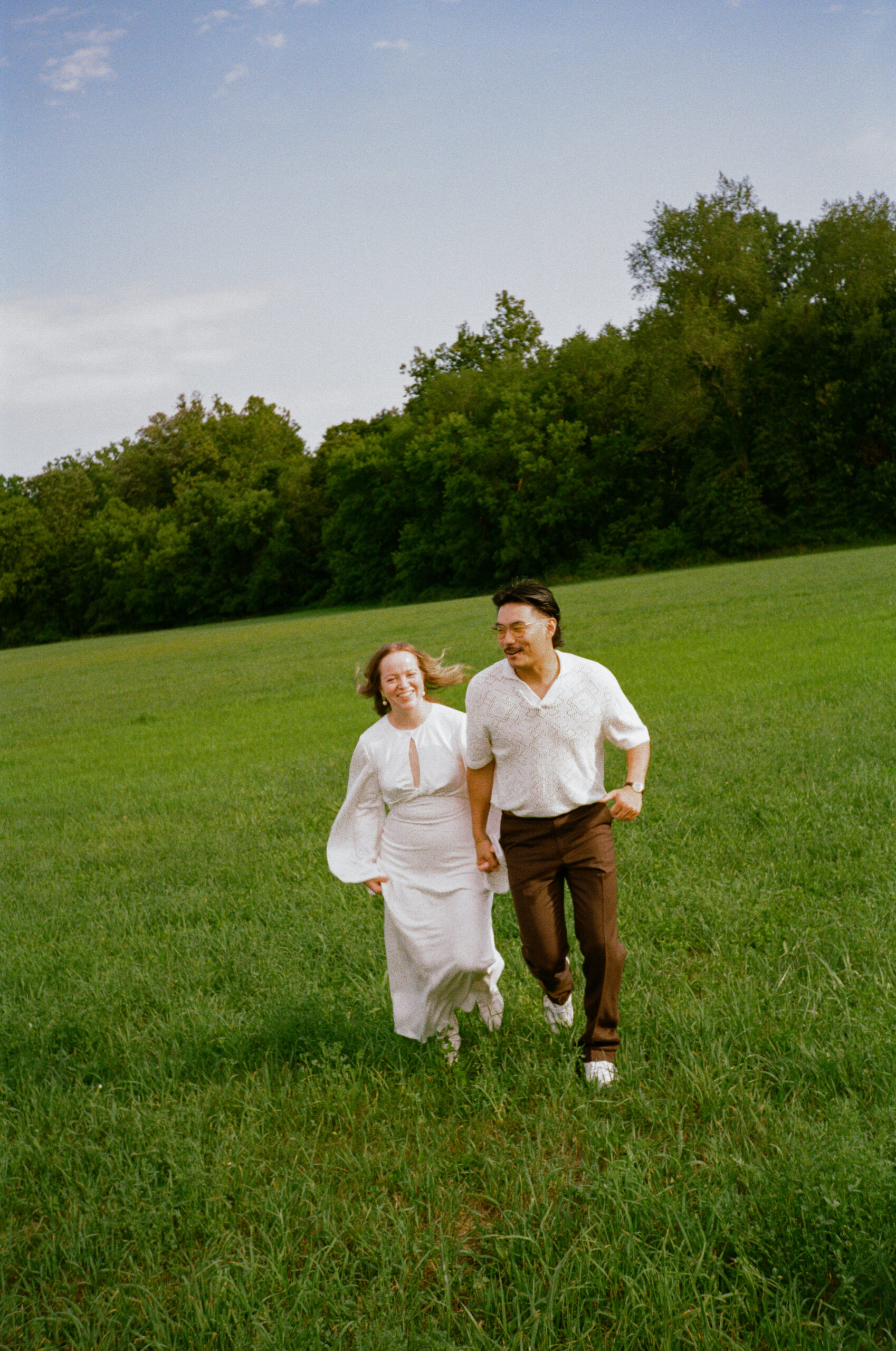 bride and groom photograph running holding hands in a field, during golden hour after their wedding reception, captured on 35mm film in indiana.
