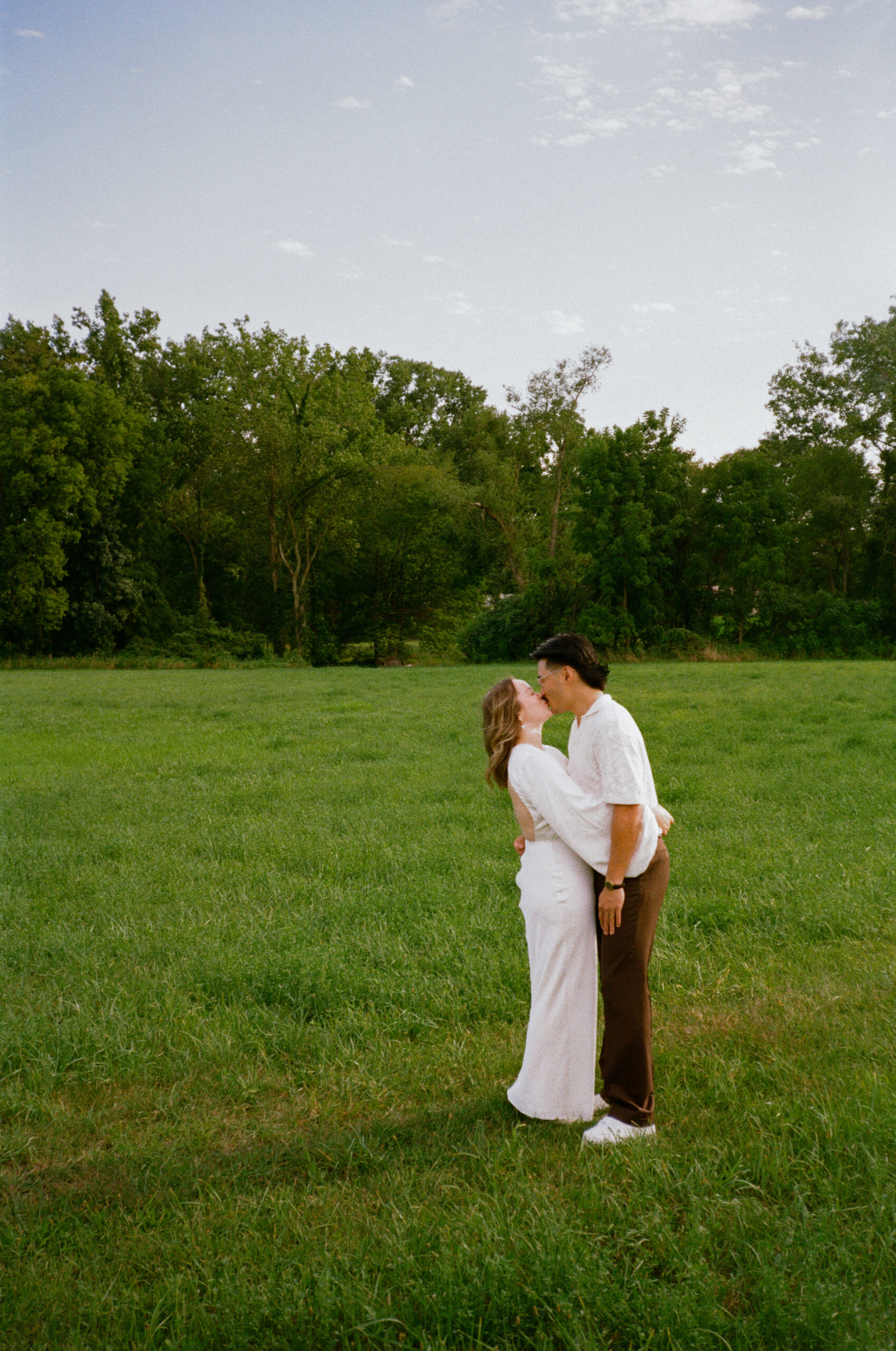 bride and groom photograph standing in a field, hugging and slow dancing during golden hour after their wedding reception, captured on 35mm film in indiana.