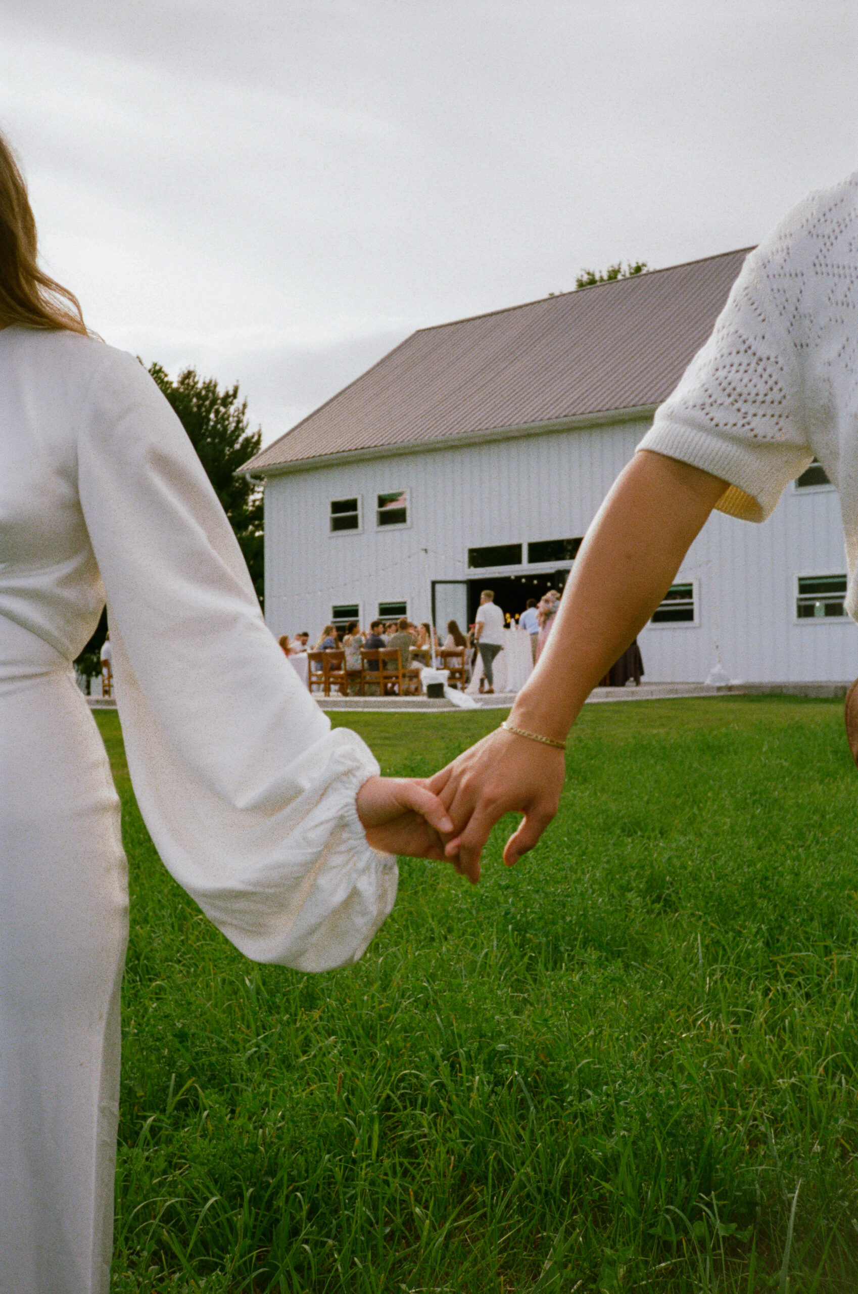 bride and groom photographs on 35mm film at their wedding reception at golden hour, a close up of their hands and rings with their reception in the background in warsaw and winona lake, indiana.