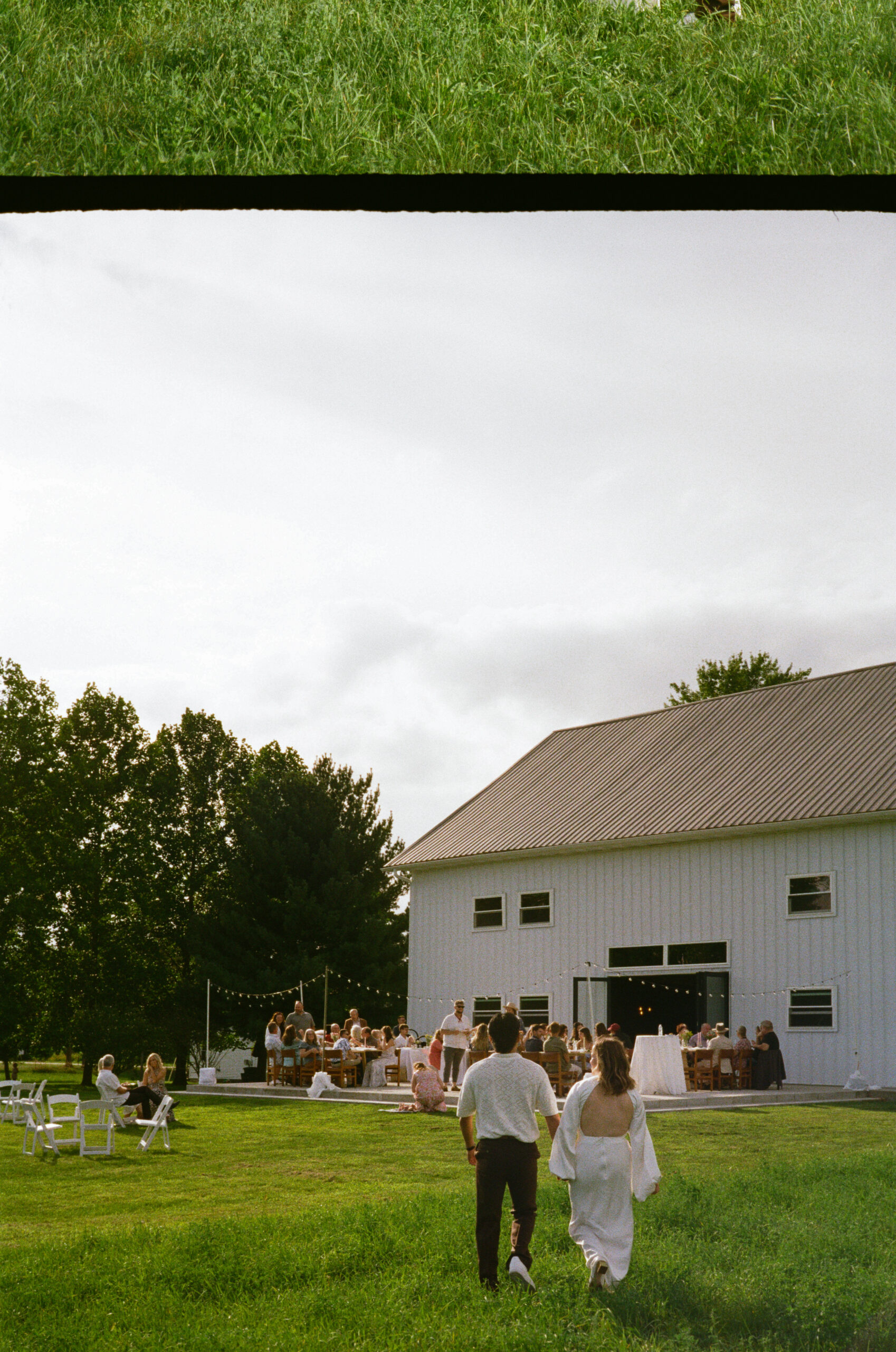 bride and groom photographs walking holding hands in a field towards outdoor reception, during golden hour after their wedding reception, captured on 35mm film in indiana.