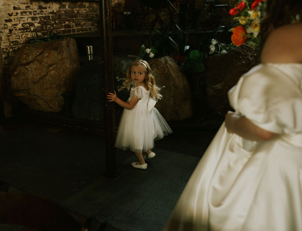 The flower girl before the wedding ceremony looks back at the bride in Muncie, Indiana at North Church Venue