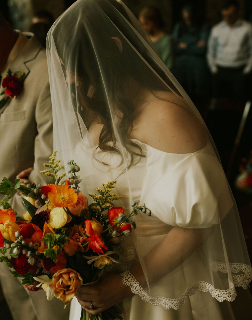 Bride with veil blusher over head as she is walked down the aisle by her dad, at her wedding ceremony at the North Church Venue in Muncie, Indiana.