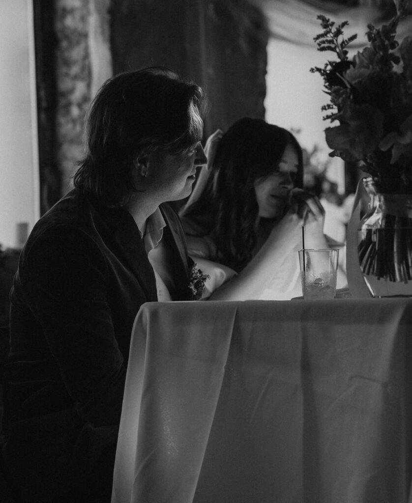 Bride wipes a tear, while sitting with groom at wedding reception during speeches at The North Church Venue in Muncie, Indiana.