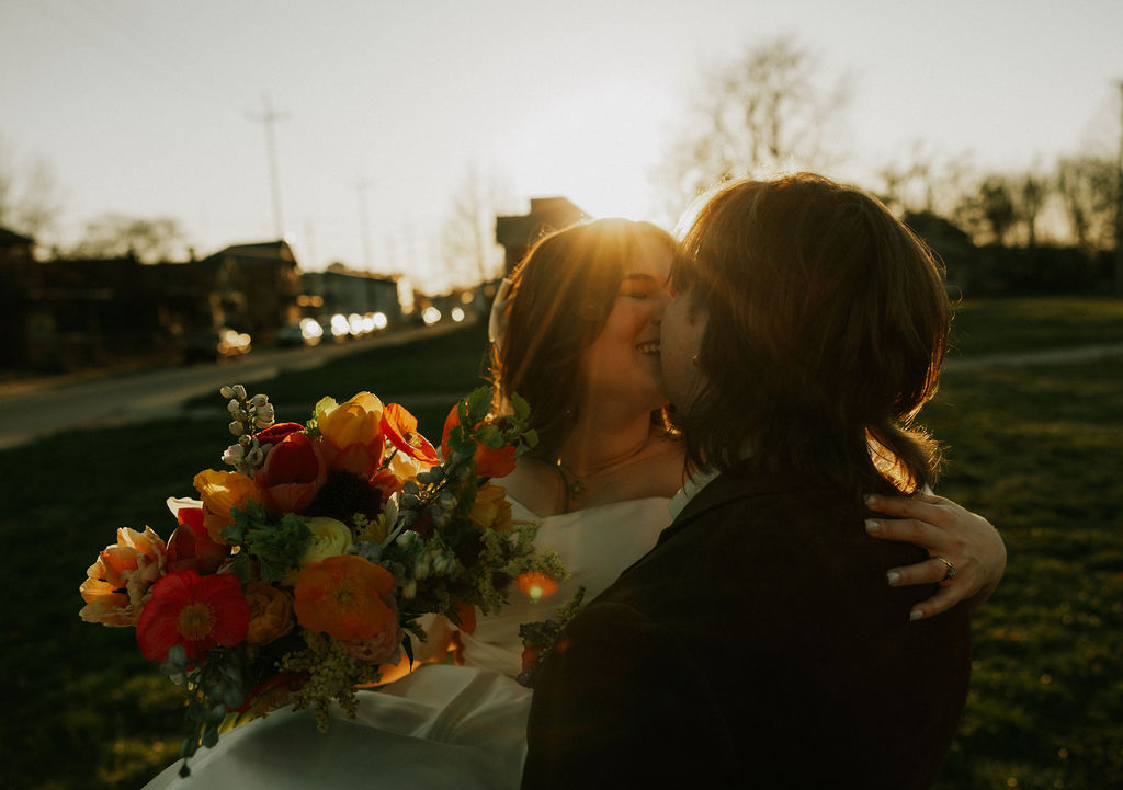 bride and groom portraits in golden hour, the groom is holding the bride in his arms as she hold her colorful bouquet in Muncie, Indiana at The North Church Venue.