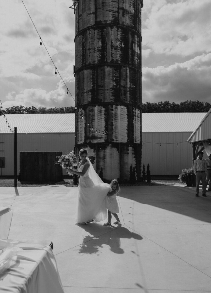 Flower girl helps bride with her dress as the bride walks around on her wedding day.