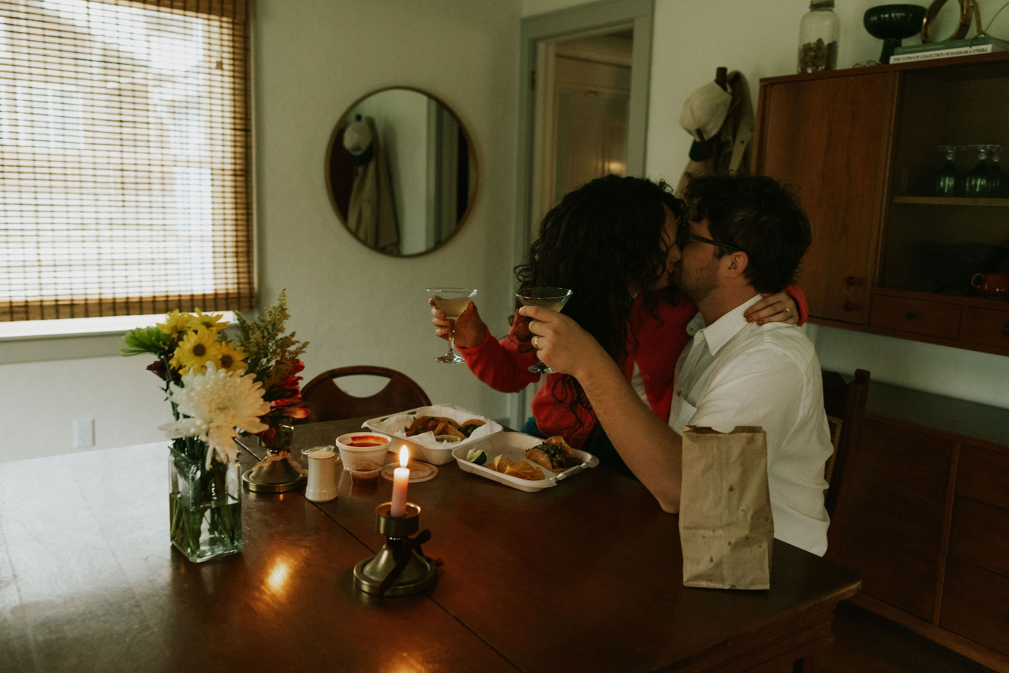 Couple cuddling at kitchen table drinking margaritas and kissing at a taco date night.