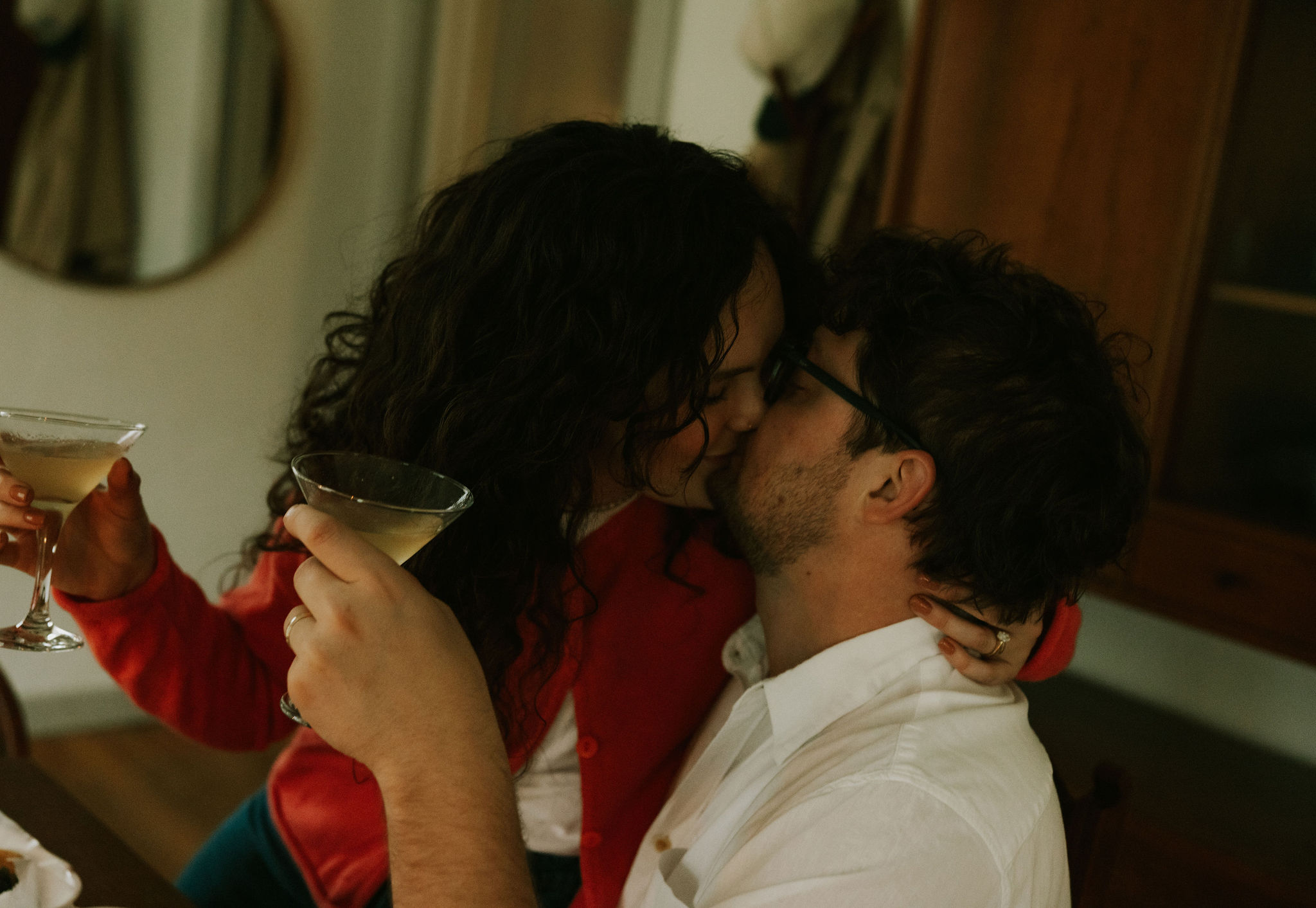 Couple cuddling at kitchen table drinking margaritas and kissing.