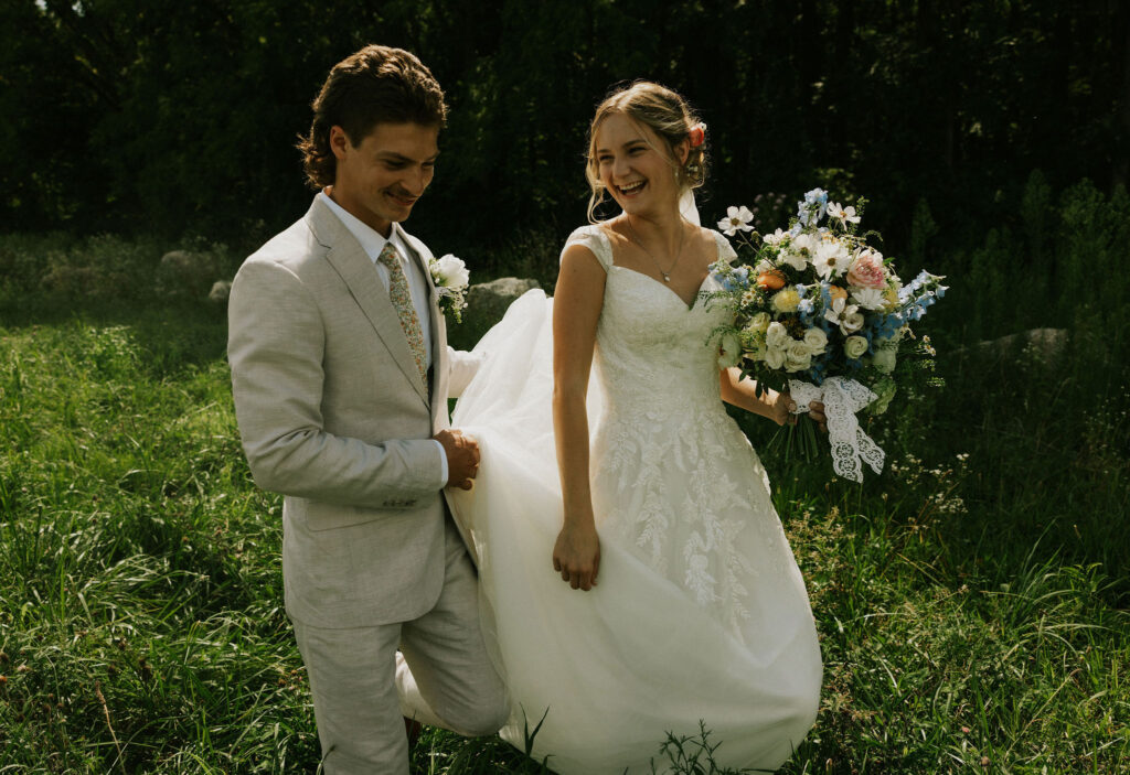 Bride and Groom walking through the grass while taking portraits, laughing at each other.