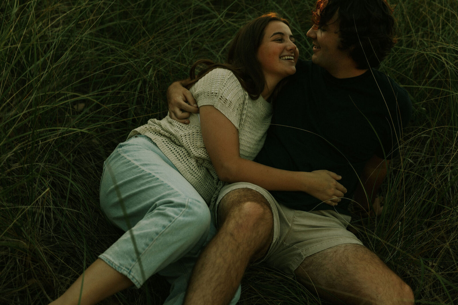 Engaged couple cuddled on the beach at Warren Dunes State Park.