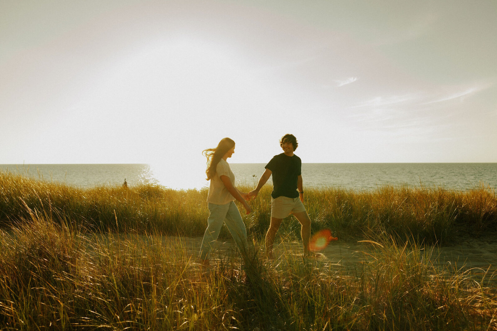 Engaged couple holding hands walking at Warren Dunes State Park.