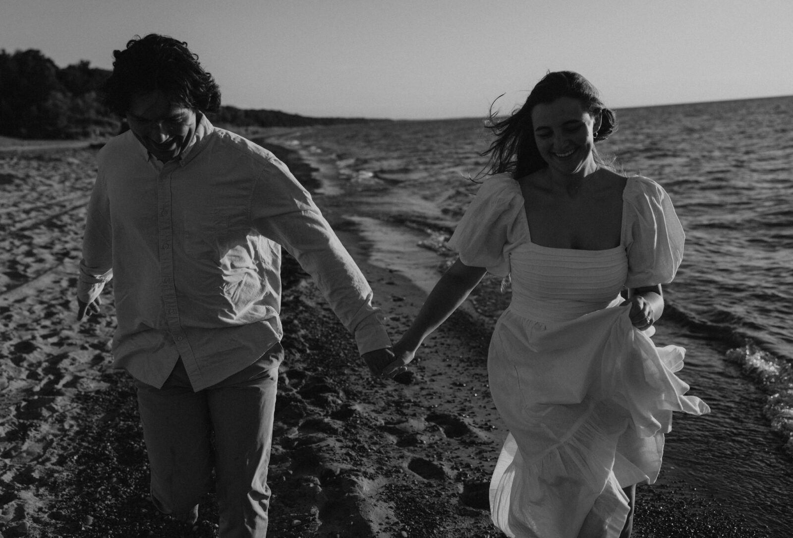 Engaged couple running on beach holding hands in Warren Dunes State Park.