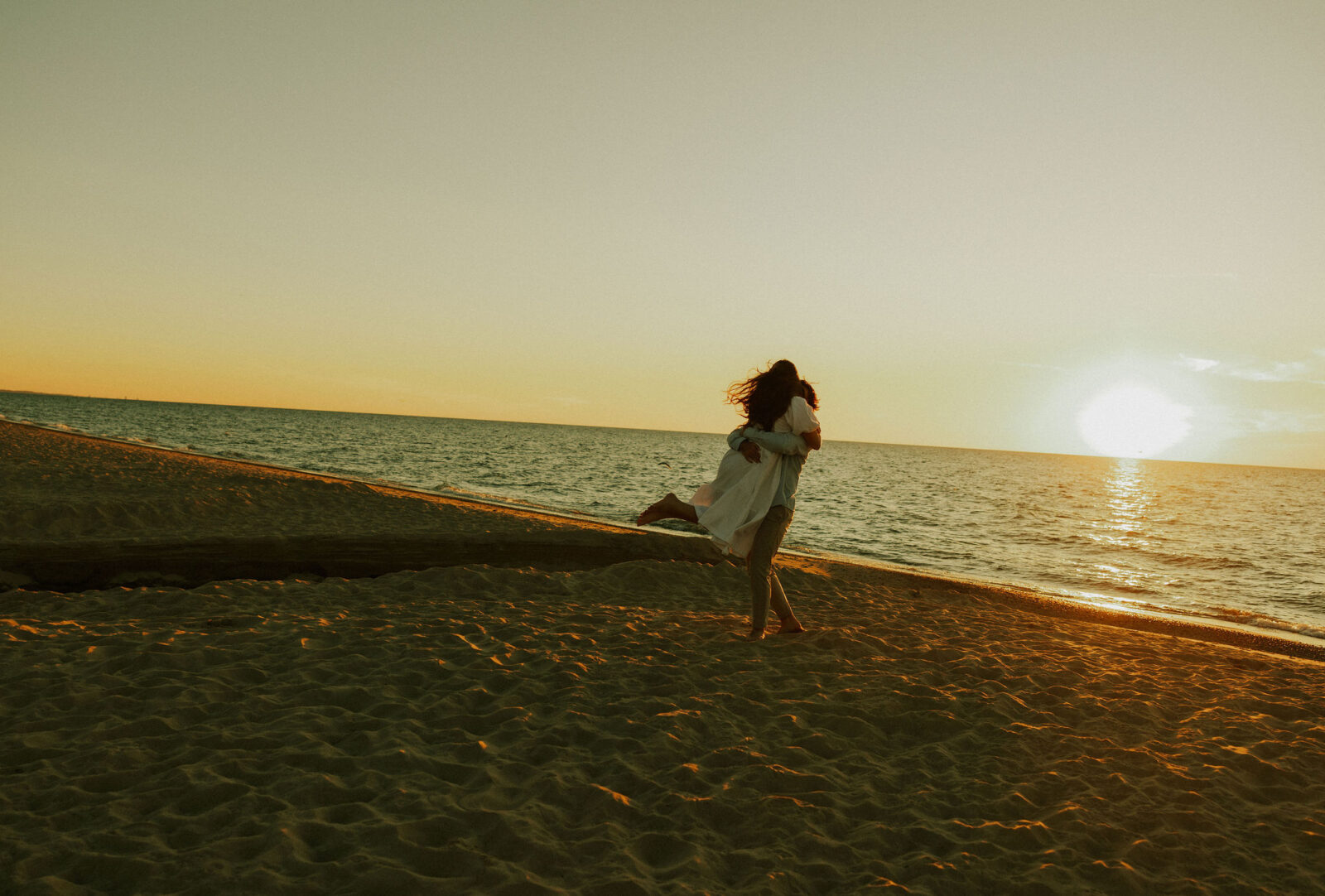 Groom picking up bride at engagement session on beach in Warren Dunes State Park.
