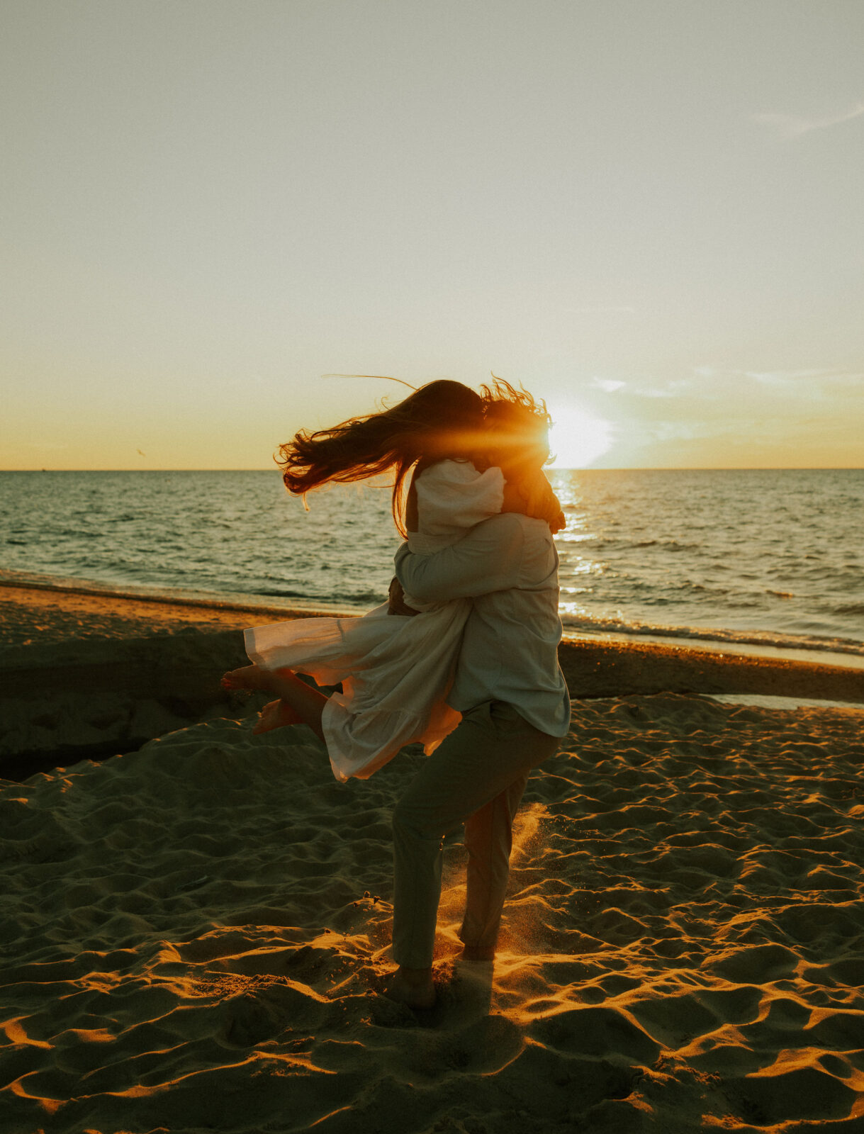 Groom picking up bride at engagement session on beach in Warren Dunes State Park.