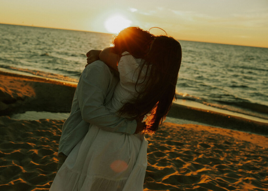 Groom picking up bride at engagement session on beach in Warren Dunes State Park.