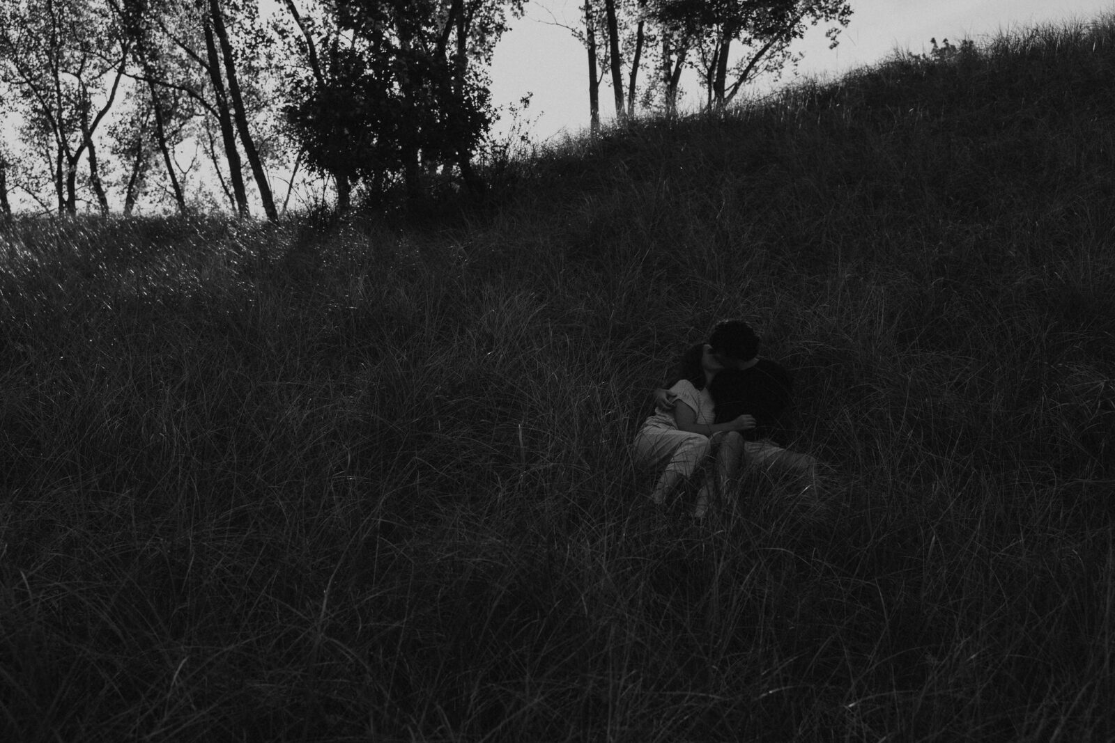 Engaged couple cuddling in the dunes at Warren Dunes State Park.